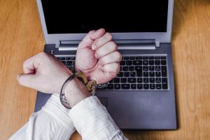 Men's hands handcuffed on a laptop. Cybersecurity law concept.